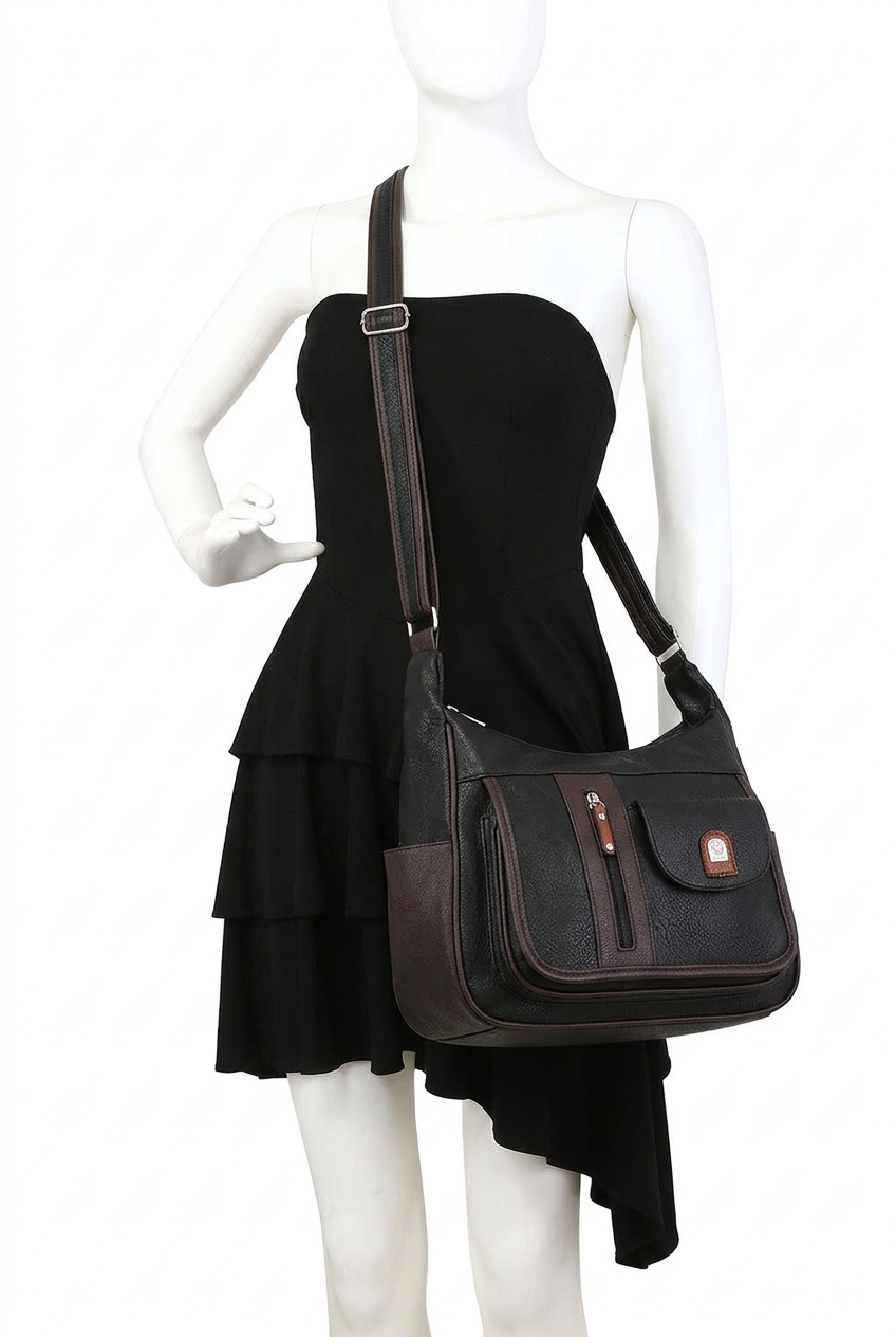 A black faux-leather shoulder bag with dark brown trim and a small brown leather logo patch, displayed on a white mannequin wearing a black dress against a white background.