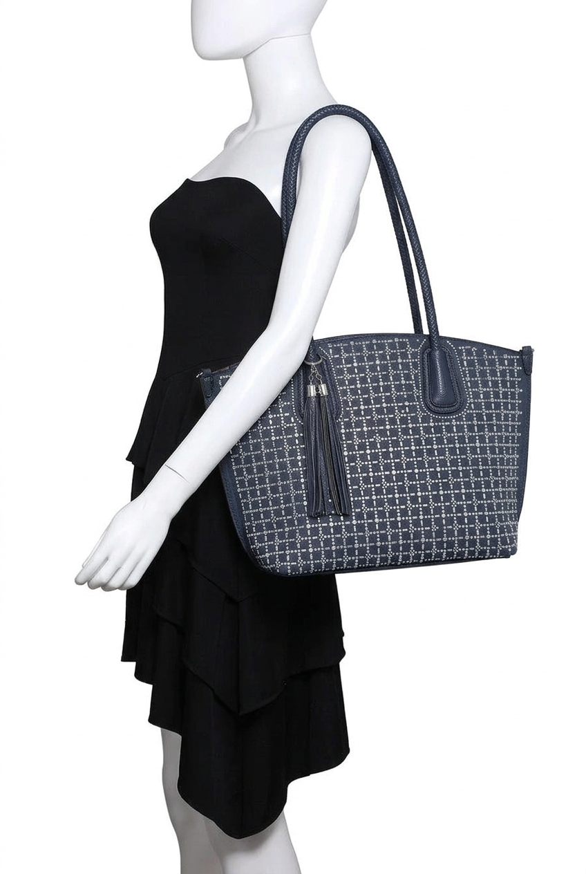 A mannequin wearing a black strapless dress is shown from the side holding a large tote bag. The bag has a dark gray and white geometric pattern, dark gray handles, and a dark gray tassel zipper pull.