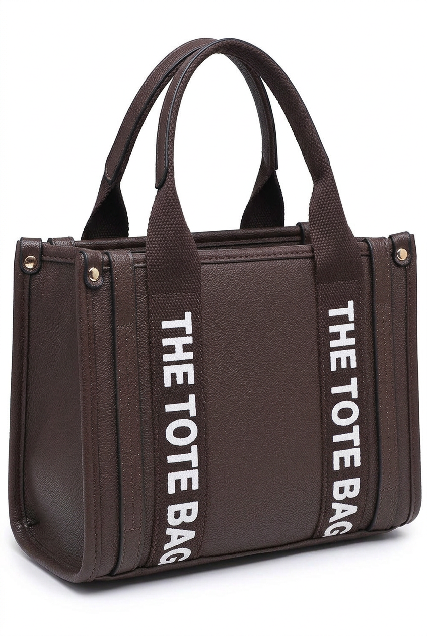 A dark brown textured tote bag with two top handles and vertical white text reading 'THE TOTE BAG' printed on the side straps, shown on a plain white background.