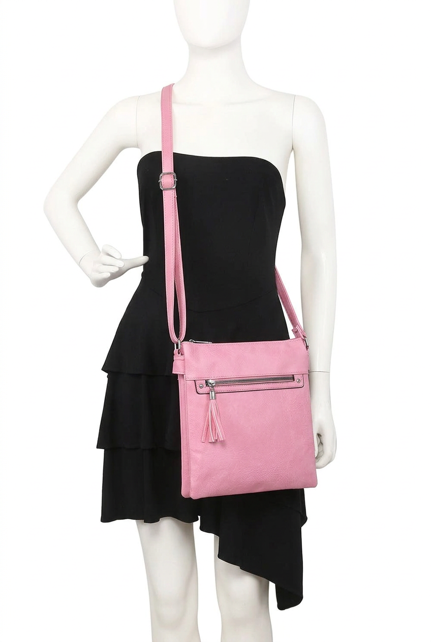 A pink crossbody bag with a front zip pocket and tassel detail, displayed on a white mannequin wearing a black dress against a white background.