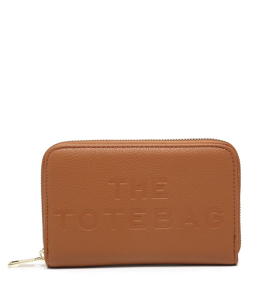 A tan pebbled zip-around wallet with 'THE TOTE BAG' embossed on the front, featuring a gold-tone zipper pull, set against a plain white background.