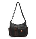 A black and dark brown faux leather shoulder bag with a front pocket, vertical zipper detail, side pockets, and a long shoulder strap, shown against a plain white background.