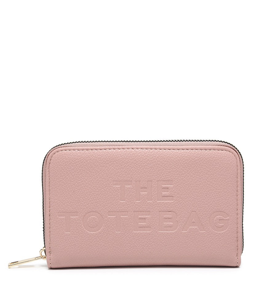 A light pink pebbled zip-around wallet with 'THE TOTE BAG' embossed on the front, featuring a gold-tone zipper pull, set against a plain white background.