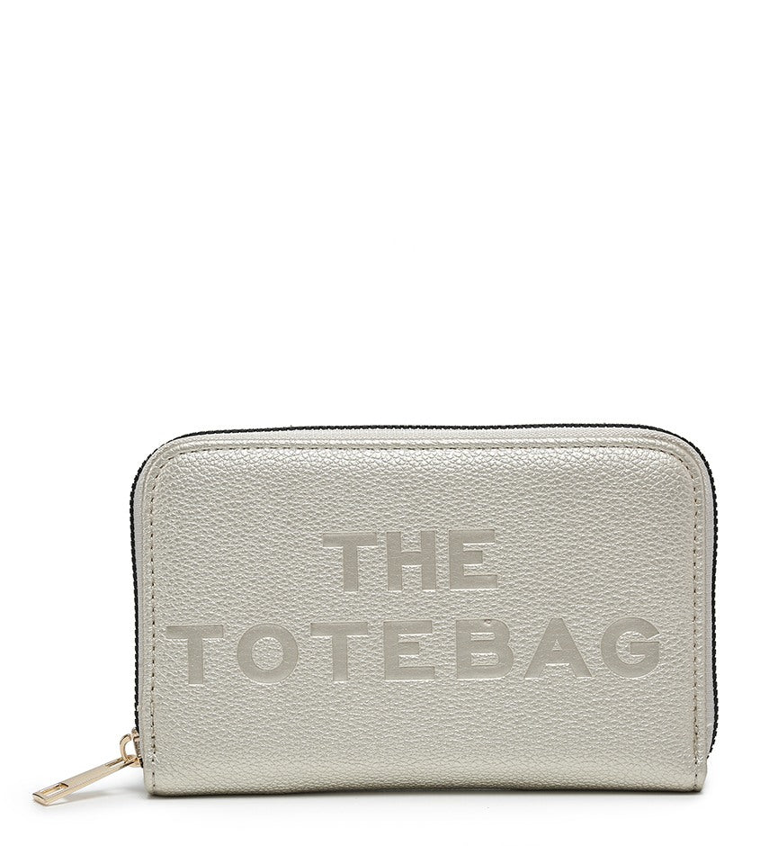 A light gray pebbled zip-around wallet with 'THE TOTEBAG' debossed on the front, shown on a plain white background.