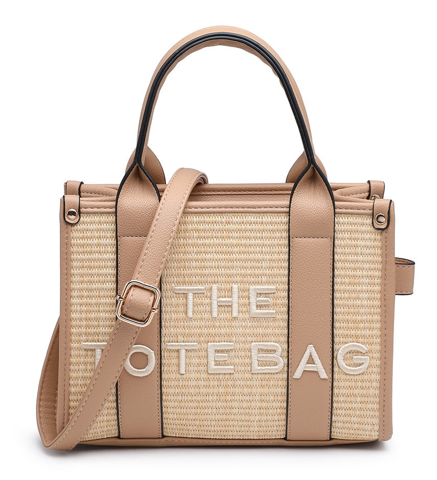 A structured tote bag with a woven beige and tan body, tan leather trim and handles, and large white embroidered text reading 'THE TOTE BAG' on the front, shown on a plain white background.